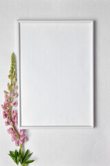 A white frame and pink flowers next to it. Mockup