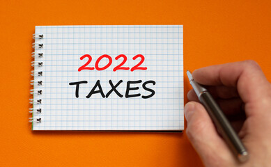 2022 taxes new year symbol. Businessman writing words '2022 taxes' on white note. Beautiful orange background. Business and 2022 taxes new year concept. Copy space.