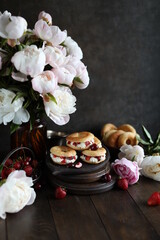 Custard rings with curd cream and berries on a dark table with a bouquet of peonies. Still life with flowers and sweets.