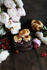 Custard rings with curd cream and berries on a dark table with a bouquet of peonies. Still life with flowers and sweets.