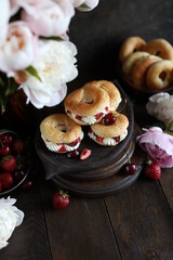 Custard rings with curd cream and berries on a dark table with a bouquet of peonies. Still life with flowers and sweets.