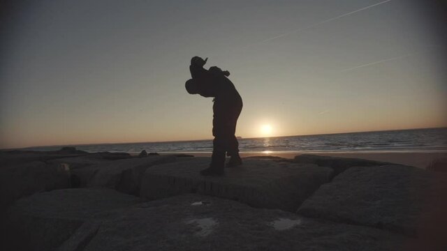Male dancer dances lowly and rises up on jetty wide shot steadicam