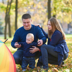 Happy family life concept. Caucasian parents (father, mother) and little son are walking, having fun and enjoying together on a sunny day. The family is resting in a green park. Family weekend.