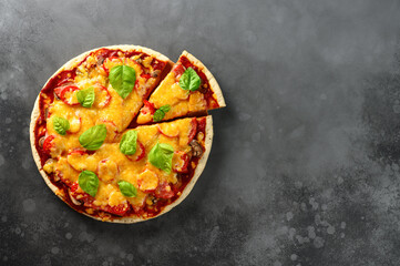 Top view of hot tasty homemade pizza with green basil leaves on the dark grey concrete background. Italian pizza on the black slate tabletop. With copy space for text. Flat lay