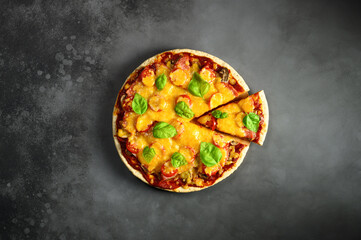 Top view of hot tasty homemade pizza with green basil leaves on the dark grey concrete background. Italian pizza on the black slate tabletop. With copy space for text. Flat lay