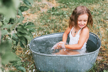 little cute girl in a pink swimsuit flops, having fun and splashing in a basin in the summer in the backyard, the concept of a happy childhood and summer vacation - obrazy, fototapety, plakaty