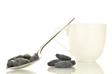 Several berries of dark purple organic honeysuckle with a metal spoon and a ceramic white cup,...