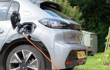 E Electric e-car on charge charging from home using a granny cable in a rural setting garden in...