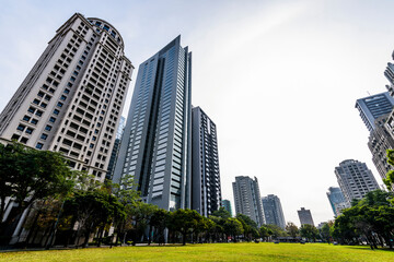Naklejka premium Low angle view of park green space and modern buildings on both sides in downtown Taichung, Taiwan.