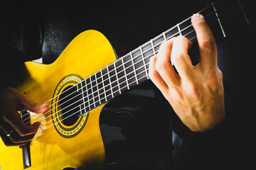 Hand of a man playing acoustic guitar. Different parts of classical guitar, such as body, strings, neck, frets. Black background