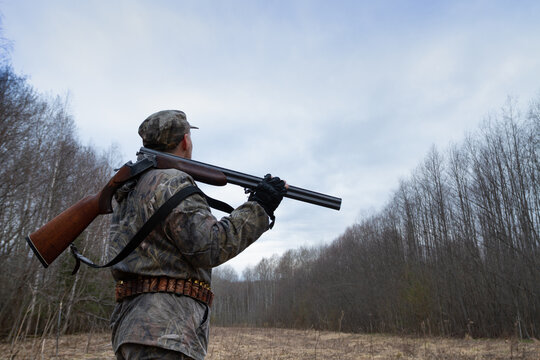 a hunter with a shotgun is waiting for a flying woodcock on a cloudy evening