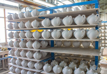 billets of ceramic white teapots in rows on the shelves in the production shop at the porcelain...