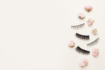 Composition with different types of false eyelashes on white background with small pink flowers roses, copy space