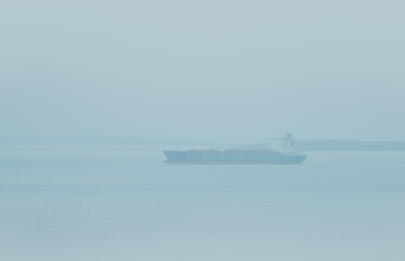 Large commercial cargo ship sailing in dense fog near the shore.