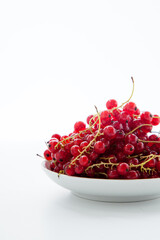 Handful of red currants in a white plate on a white background