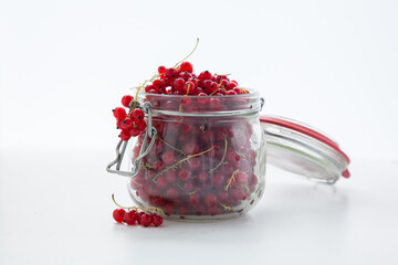Handful of red currants in an open glass jar on a white background