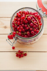 Handful of red currants in an open glass jar on a wooden background