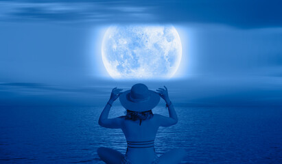 A beautiful young girl sitting by the sea and watching blue moon "Elements of this image furnished by NASA " © muratart