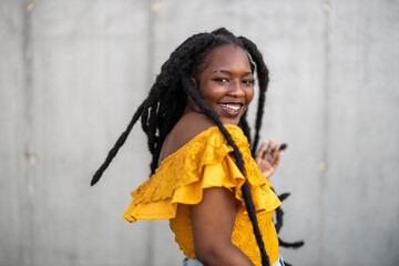 Beautiful young woman dancing in front of gray wall 
