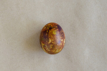 One egg, painted in brown colors, on kraft paper. Minimalism concept. Unusual pattern on surface of egg in form of blurred spots, handmade. Top view. Copy space.