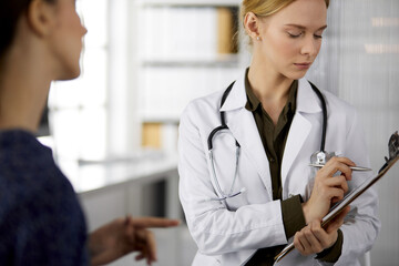 Friendly smiling female doctor and patient woman discussing current health examination while...