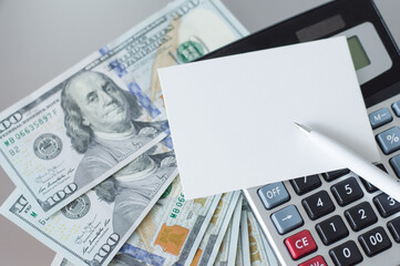 blank white business card on the calculator lies next to money and white pen on the table, business and finance concept