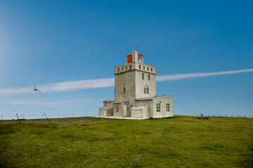 Fototapeta na wymiar White lighthouse with flying puffin on Dyrhólaey view point, Iceland 