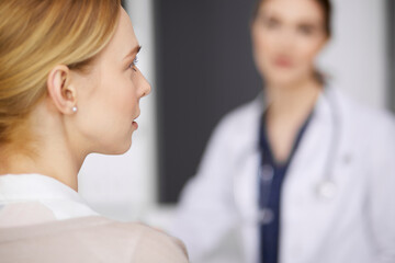 Friendly smiling female doctor and patient woman discussing current health examination while sitting in clinic. Perfect medical service in hospital. Medicine concept