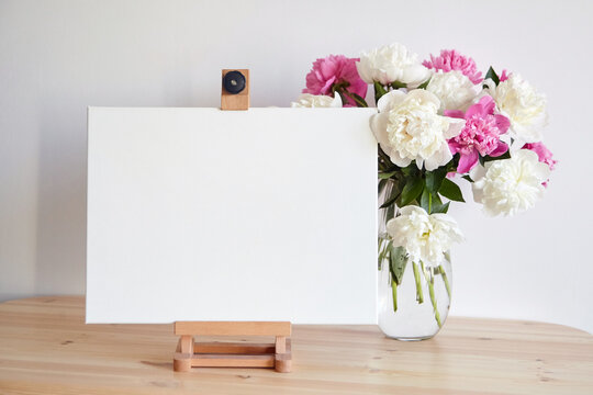 Canvas mockup on easel and pink flowers on wooden table on white wall background