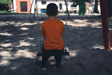 Sad boy sitting  alone on the swing in the playground