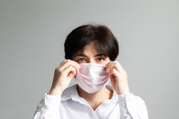 Woman in white shirt with short hair and dark hair looking at the camera on a medical mask, bust portrait, frontal photography, daylight. High quality photo