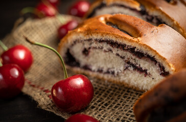Bun with poppy seeds and fresh cherries on a wooden background