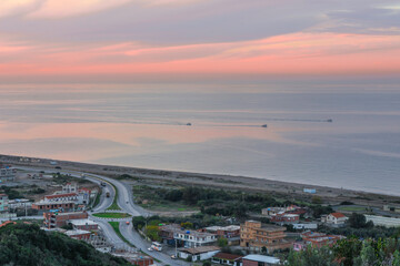 Aerial view of a highway near the beach in the Mediterranean Sea, a roundabout road near the coast and three fishing boats in the sea at sunset, a coastal village in Jijel Province, Algeria, Africa.