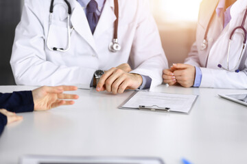 Unknown male doctor listening to his patient woman while sitting in sunny clinic. Medicine concept during Coronavirus pandemic. Covid 2019