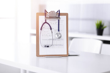 Stethoscope and clipboard with medication history records are on the table at sunny doctor's working place. Medicine concept