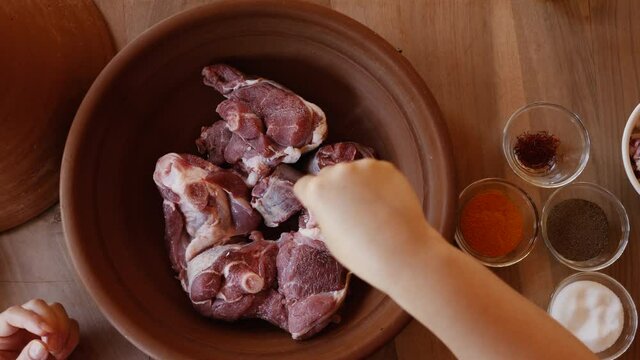 Cooking a lamb, mutton, sheep meat tajine, tagine in a Moroccan clay pot, seasoning the meat fillets with fresh spices including Saffron. Traditional Moroccan slow-cooked food.