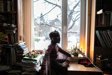 A child in profile in full growth in a playful brown suit of a character on a windowsill in daylight, at home, shooting from the side, a general plan