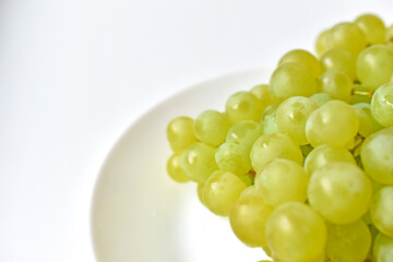 Green juicy delicious grapes on a white plate