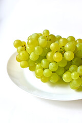 Green juicy delicious grapes on a white plate