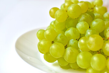 Green juicy delicious grapes on a white plate