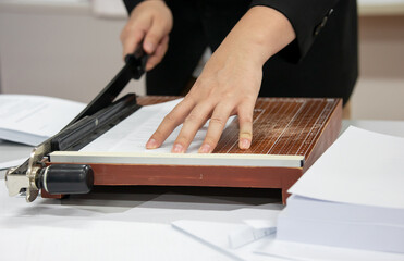 A young man using a Paper cutter or guillotine to make a book in the office. cutting paper on desk....