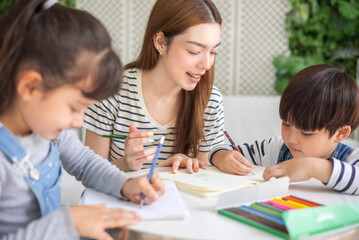 happy loving family. pretty young mother reading a book and drawing to her daughter and son.Mother teach Asian preschool student do homework by reawing by a color.