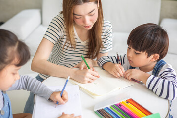 happy loving family. pretty young mother reading a book and drawing to her daughter and son.Mother teach Asian preschool student do homework by reawing by a color.