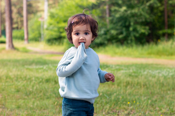 A little caucasian child walks in nature. A cute baby girl holds a sweater sleeve in her mouth....