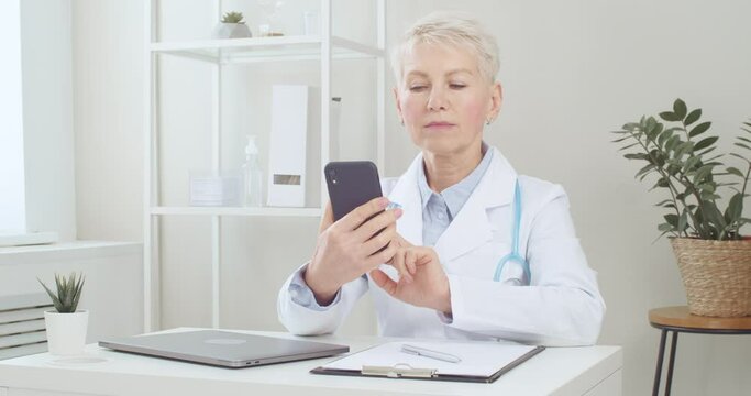 
Senior doctor making video call online using mobile phone and remote telehealth app. Telemedicine or virtual healthcare
