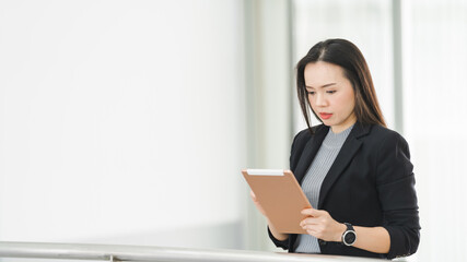 Portrait of a cheerful confident Asian businesswoman in a business suit standing whie using a digital tablet in the business building. Business stock photo