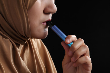Close up young muslim woman smoking e-cigarette on black background