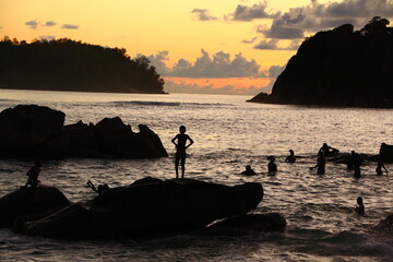 Silhouette of a group of teenage children swimming in the sea jumping diving playing in the water on the rocks at sunset. Happy childhood concept. Background image. Summer landscape
