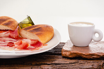 Desayuno mediterráneo, taza de café y plato con pan, envase monodosis de aceite de oliva y jamón ibérico