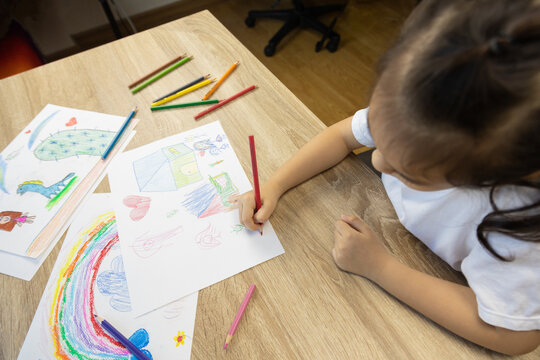 Top view shot of mother and daughter are drawing and coloring beautiful rainbow picture on paper together shows concept of art playing which enhance creativity, learning and enjoyment for child.